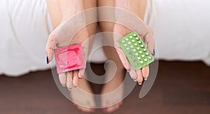 Young beautiful woman holding birth control pills and condom at bedroom