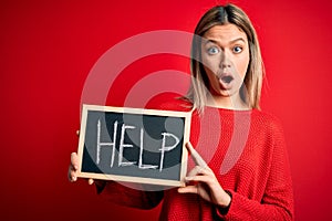 Young beautiful woman holding blackboard standing over isolated red background scared in shock with a surprise face, afraid and