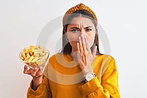 Young beautiful woman holding bowl with macaroni pasta over isolated white background cover mouth with hand shocked with shame for