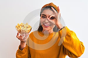 Young beautiful woman holding bowl with macaroni pasta over isolated white background with happy face smiling doing ok sign with