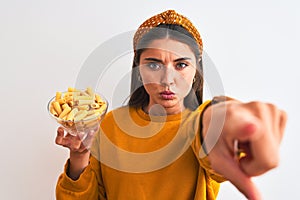 Young beautiful woman holding bowl with macaroni pasta over isolated white background pointing with finger to the camera and to