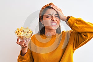 Young beautiful woman holding bowl with macaroni pasta over isolated white background stressed with hand on head, shocked with