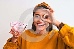 Young beautiful woman holding bowl with marshmallows over isolated white background with happy face smiling doing ok sign with