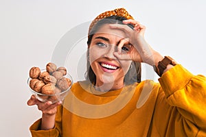 Young beautiful woman holding bowl with walnuts standing over isolated white background with happy face smiling doing ok sign with