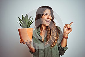 Young beautiful woman holding cactus pot over white isolated background very happy pointing with hand and finger to the side