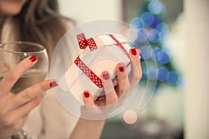 Young beautiful woman holding Chrismtas present in her hands in front of a beautifully decorated Christmas tree