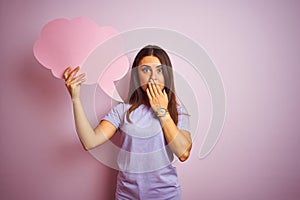Young beautiful woman holding cloud speech bubble over isolated pink background cover mouth with hand shocked with shame for