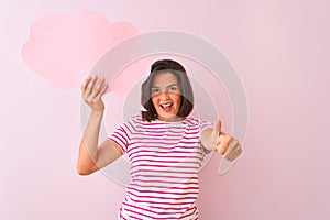 Young beautiful woman holding cloud speech bubble standing over isolated pink background happy with big smile doing ok sign, thumb