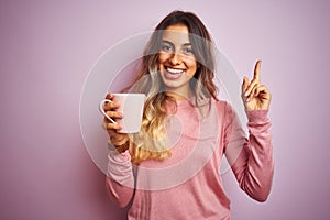 Young beautiful woman holding cup of coffee over pink isolated background very happy pointing with hand and finger to the side