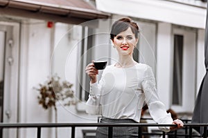 Young beautiful woman holding a cup of coffee or tea in cafe, restaurant. Brunette girl is drinking hot drinks, looking