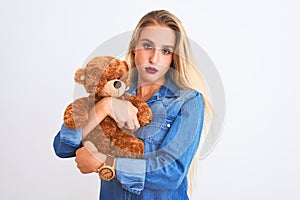 Young beautiful woman holding cute teddy bear standing over isolated white background with a confident expression on smart face