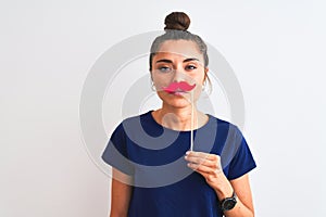 Young beautiful woman holding fanny party mustache over isolated white background with a confident expression on smart face