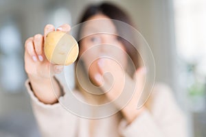 Young beautiful woman holding fresh potato at home cover mouth with hand shocked with shame for mistake, expression of fear,