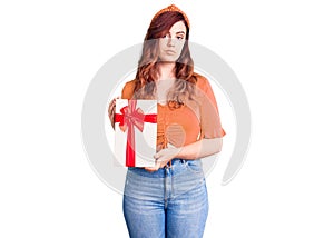 Young beautiful woman holding gift thinking attitude and sober expression looking self confident