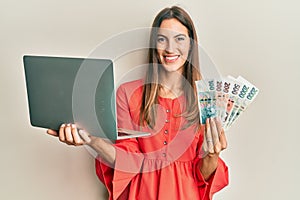 Young beautiful woman holding laptop and czech koruna banknotes smiling with a happy and cool smile on face