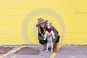 Young beautiful woman holding and loving her dog. Yellow brick wall background. Love and pets outdoors