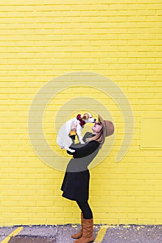 Young beautiful woman holding and loving her dog. Yellow brick wall background. Love and pets outdoors