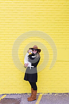 Young beautiful woman holding and loving her dog. Yellow brick wall background. Love and pets outdoors