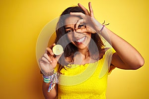 Young beautiful woman holding middle lemon standing over isolated yellow background with happy face smiling doing ok sign with