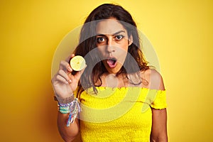 Young beautiful woman holding middle lemon standing over isolated yellow background scared in shock with a surprise face, afraid