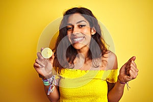 Young beautiful woman holding middle lemon standing over isolated yellow background screaming proud and celebrating victory and