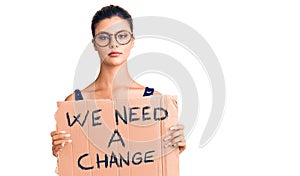 Young beautiful woman holding we need a change banner thinking attitude and sober expression looking self confident