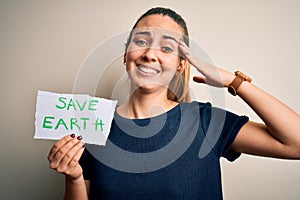 Young beautiful woman holding paper asking for save earth and enviroment conservation stressed with hand on head, shocked with