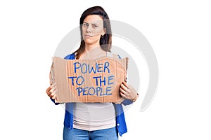 Young beautiful woman holding power to the people banner thinking attitude and sober expression looking self confident