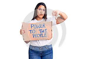 Young beautiful woman holding power to the people cardboard banner with angry face, negative sign showing dislike with thumbs