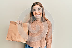 Young beautiful woman holding take away paper bag looking positive and happy standing and smiling with a confident smile showing