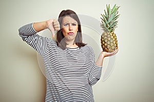 Young beautiful woman holding tropical fruit pineapple over isolated background with angry face, negative sign showing dislike