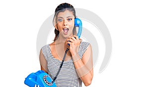 Young beautiful woman holding vintage telephone scared and amazed with open mouth for surprise, disbelief face