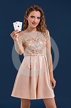 Young beautiful woman holding the winning combination of poker cards on dark blue background. Two aces