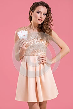 Young beautiful woman holding the winning combination of poker cards on pink background. Two aces