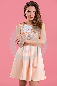 Young beautiful woman holding the winning combination of poker cards on pink background. Two aces