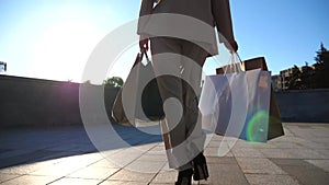 Young beautiful woman holds shopping bags walking at sunny city street after purchases. Fashionable girl carries paper