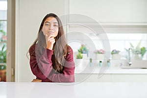 Young beautiful woman at home looking confident at the camera with smile with crossed arms and hand raised on chin