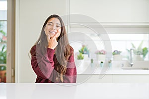 Young beautiful woman at home looking confident at the camera with smile with crossed arms and hand raised on chin