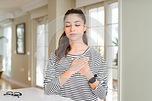 Young beautiful woman at home smiling with hands on chest with closed eyes and grateful gesture on face