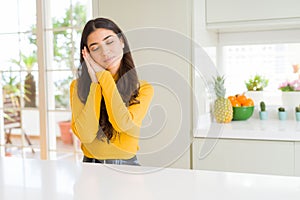 Young beautiful woman at home on white table sleeping tired dreaming and posing with hands together while smiling with closed eyes