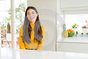 Young beautiful woman at home on white table winking looking at the camera with sexy expression, cheerful and happy face