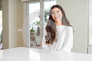 Young beautiful woman at home on white table winking looking at the camera with sexy expression, cheerful and happy face