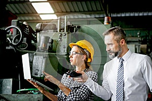 Young beautiful woman industrial engineer worker with helmet and safety glasses using laptop computer during discussing with