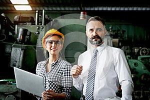 Young beautiful woman industrial engineer worker with helmet and safety glasses using laptop computer during discussing with