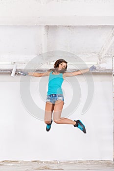 Young beautiful woman jump and paints the wall with white paint