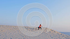 Young beautiful woman jumping, doing exercises on balance and coordination, on the sand, on a deserted beach, in summer
