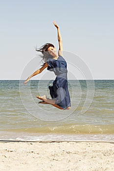 Young beautiful woman jumping at seaside in blue dress