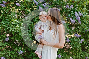 Young beautiful woman kisses baby girl in the cheek in summer