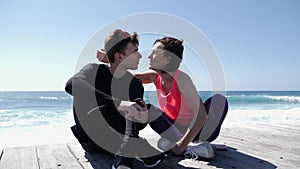 Young beautiful woman kisses fit sportive man in the cheek near the ocean