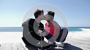 Young beautiful woman kisses fit sportive man in the lips near the ocean.